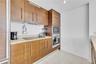 Wood-finish cabinetry with metallic pulls, solid surface countertops, built-in stainless steel wall oven and microwave, and large-format tile flooring