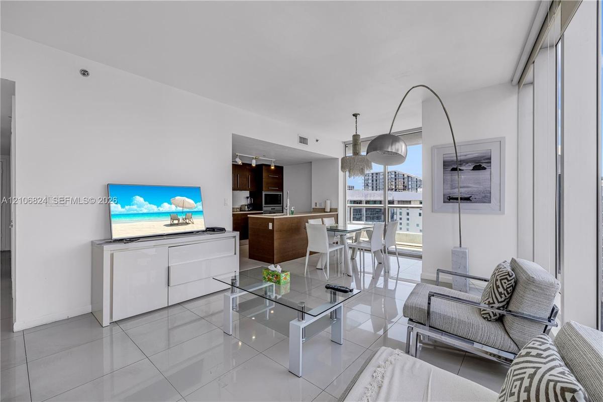 Floor-to-ceiling glass windows, polished tile flooring, kitchen with wood-finish cabinetry, and pendant lighting