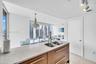 Kitchen island featuring stone countertops, undermount double-basin stainless steel sink, wood-finish cabinetry with metallic hardware, and overhead t