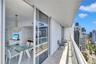 Covered balcony with stone tile flooring and metal railings, featuring sliding glass doors and high-rise urban scenery