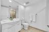 Bathroom featuring a white integrated vanity with a molded sink, expansive wall-mounted mirror, stone-tile flooring, and a glass-enclosed shower