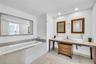Bathroom featuring dual circular vessel sinks, stone-surfaced vanity with wooden cabinetry, large inset soaking tub with stone tile surround, and expa