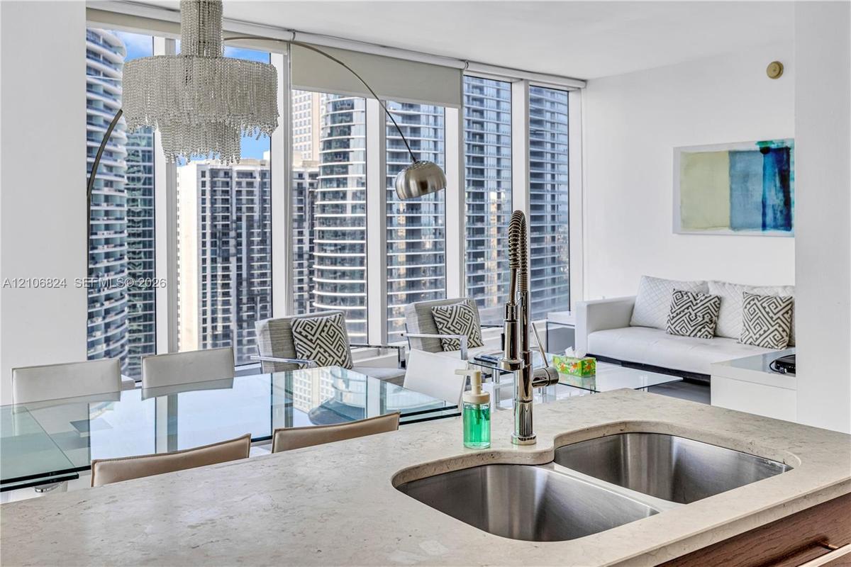 Floor-to-ceiling windows, stone-surfaced kitchen island with a double-basin stainless steel sink, and high-rise urban scenery