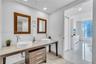 Dual-basin vanity featuring stone countertop, white vessel sinks, wood-finish cabinetry, and chrome fixtures