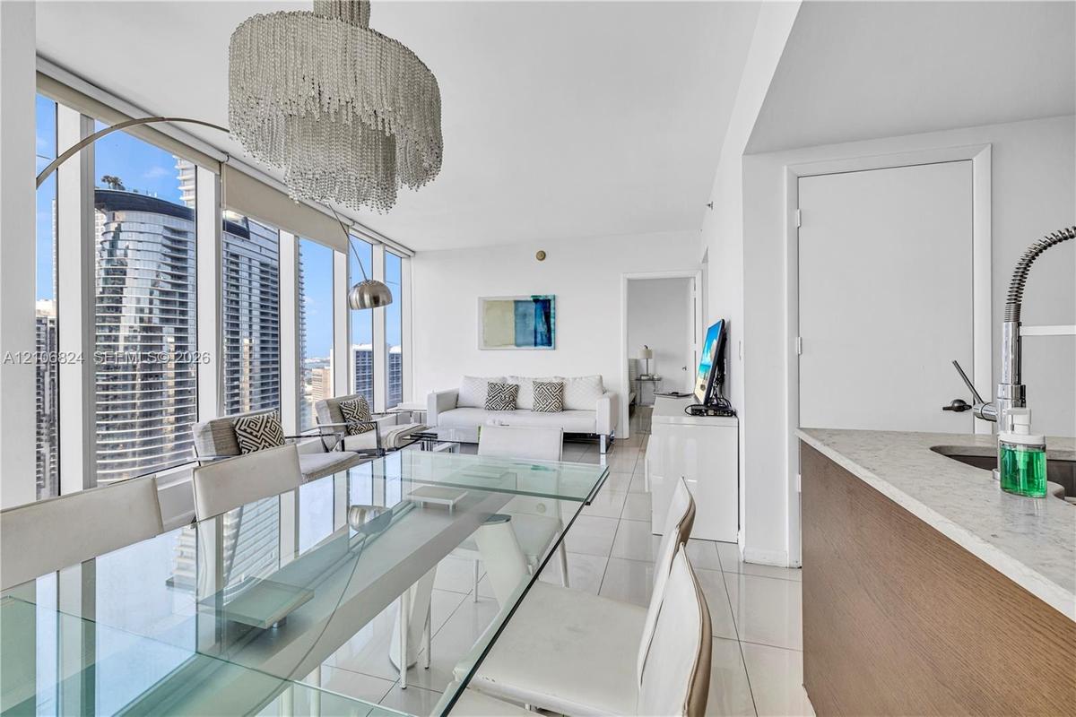 Floor-to-ceiling windows, tile flooring, tiered crystal chandelier, kitchen peninsula with stone-finish countertop, and stainless steel pull-down fauc
