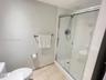 Walk-in shower with sliding glass doors, adjustable handheld shower fixture, light-toned tile flooring, and wall-mounted chrome hardware