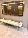 Dual elevator bank featuring metallic gold doors, wall-mounted control panel, large rectangular decorative mirror with beveled edges, and polished ter