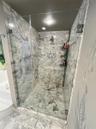 Walk-in shower with floor-to-ceiling natural stone tile, frameless glass enclosure, polished chrome hardware, and recessed lighting