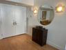 Double-door entry featuring brass hardware, wood-finish flooring, two ornate wall-mounted sconces, and a large circular wall mirror