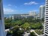 Elevated coastal perspective featuring expansive water and skyline scenery, mature tropical landscaping, and paved arrival court