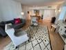 Open-concept interior featuring light wood-finish flooring, decorative ceiling pendant lighting, dual wall-mounted sconces, and double-entry doors