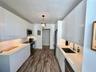 Galley kitchen featuring flat-panel white cabinetry, solid-surface countertops, stainless steel appliances, under-cabinet lighting, and wood-finish fl