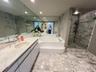 Bathroom featuring a stone vanity countertop with an integrated oval sink, full-width wall mirror, oversized soaking tub with a stepped entry, and a w