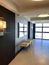 Large-format tile flooring, recessed tray ceiling, floor-to-ceiling windows, dark wood-finish wall paneling, and wall-mounted light fixtures