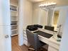 Built-in vanity with stone-surfaced countertop, large wall-mounted mirror, multi-bulb vanity lighting, and integrated shelving unit with wood-finish f