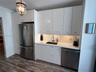 Kitchen area featuring flat-panel white cabinetry, solid-surface countertops, integrated stainless steel appliances, undermount sink with a gooseneck 