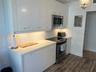Kitchen featuring flat-panel cabinetry, light-toned countertops, under-cabinet lighting, stainless steel appliances, and wood-finish flooring