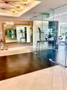 Floor-to-ceiling glass enclosure with stainless steel hardware, gold-tone geometric ceiling lighting, large-format wall mirror, and contrasting tile f