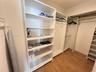 Walk-in storage space featuring built-in white shelving units, integrated hanging rods, and wood-finish flooring