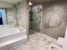 Bathroom featuring a soaking tub with a tiered surround, a glass-enclosed shower with stone-tile surround, and stone-tile flooring