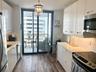 Galley kitchen featuring high-gloss white cabinetry, solid-surface countertops, wood-finish flooring, stainless steel appliances, and a glass-paneled 