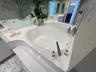 Oval soaking tub with a deck-mounted faucet and hand shower, set into a solid-surface surround, complemented by a large wall-to-wall mirror and natura