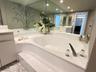 Oval soaking tub with integrated deck, large-format wall-to-wall mirror, built-in cabinetry, and tile flooring