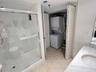 Glass-enclosed shower with tiled surround, stone-top vanity with undermount sink, and integrated laundry closet with louvered doors and stackable wash