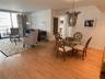 Open-concept living space featuring wood-finish flooring, floor-to-ceiling glass paneling with balcony access, and an ornate, suspended metal chandeli
