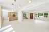 Open-concept interior featuring wood-finish cabinetry, a central kitchen island, large-format tile flooring, a floating staircase with glass railing, 