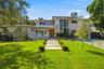 Modern exterior featuring a metal roof, stone facade accents, expansive floor-to-ceiling windows, a wood-finish front door, and a geometric concrete p