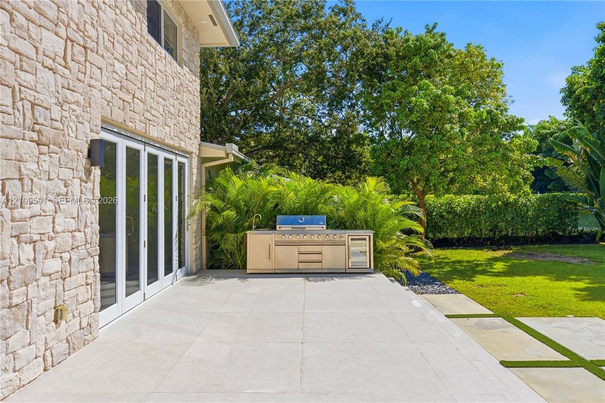 Outdoor terrace featuring a stacked stone exterior, large-format stone pavers, and a built-in stainless steel kitchen with a grill and integrated refr