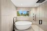 Freestanding soaking tub with matte black floor-mounted faucet, walk-in shower with glass enclosure, rain shower head, and floor-to-ceiling textured t