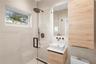 Modern bathroom featuring large-format wall tiling, a floating wood-finish vanity with a rectangular vessel sink, matte black hardware, and a glass-en