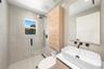 Walk-in shower with a glass enclosure and wall-mounted matte black rainfall shower head, wood-finish wall-mounted cabinetry, wall-mounted rectangular 