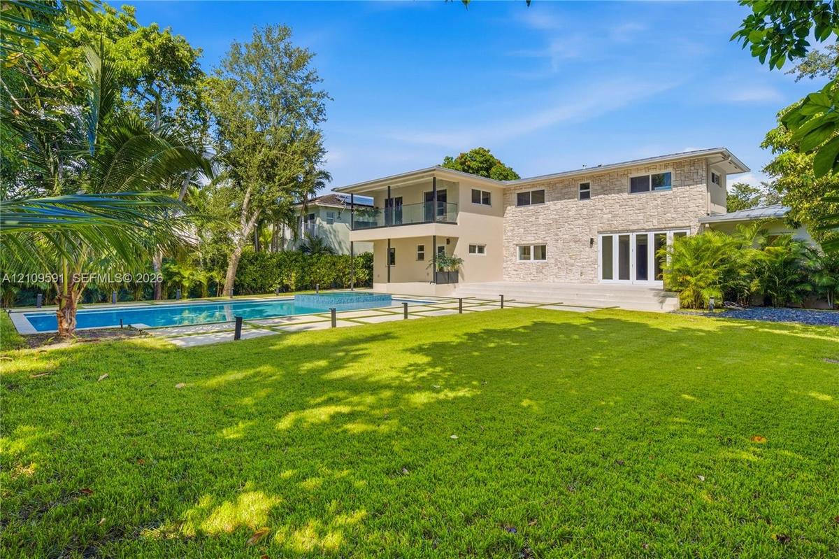 Exterior facade featuring stone veneer cladding, swimming pool with integrated spa, glass-panel balcony railing, and manicured lawn