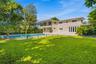 Exterior facade featuring stone veneer cladding, swimming pool with integrated spa, glass-panel balcony railing, and manicured lawn