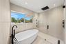 Freestanding soaking tub with matte black floor-mounted faucet, walk-in shower with frameless glass enclosure, rainfall showerhead, and neutral wall t