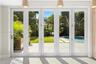 Multi-panel white-frame glass doors, stone patio, swimming pool, manicured lawn, and suspended pendant lighting
