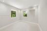 Neutral interior space featuring recessed ceiling lighting, light-toned flooring, two windows, and a wall-mounted ductless air conditioning unit