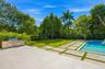 Backyard featuring a swimming pool, integrated stainless steel outdoor kitchen, stone paver patio with turf inlays, and mature landscaping