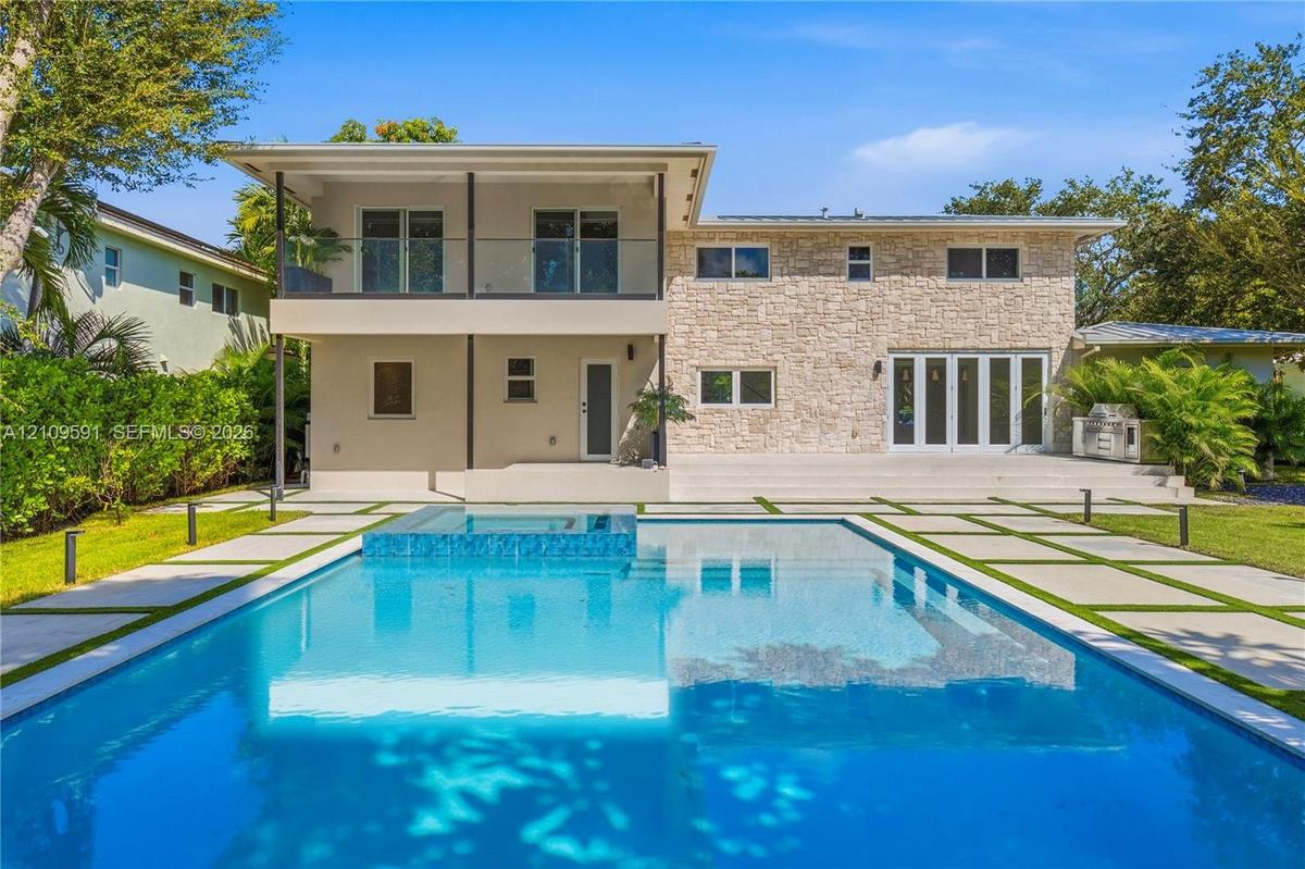Exterior facade featuring stone veneer cladding, a second-level balcony with glass railing, a rectangular swimming pool with an integrated spa, and co