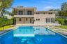 Exterior facade featuring stone veneer cladding, a second-level balcony with glass railing, a rectangular swimming pool with an integrated spa, and co