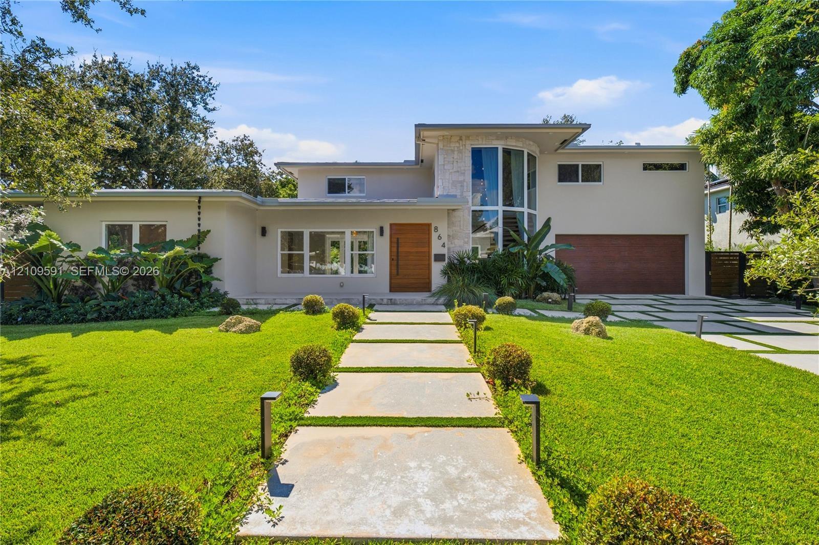 Modern exterior featuring a prominent two-story glass tower, custom horizontal wood-paneled entry door, geometric concrete paver walkway, and stone ac