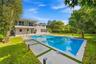 Backyard featuring a rectangular swimming pool, concrete paver decking, manicured lawn, stone-veneer exterior finish, and a second-level balcony with 