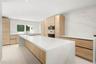 Modern kitchen featuring light wood-finish cabinetry, a waterfall-edge center island, solid-surface countertops, and full-height stone backsplash