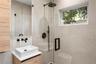 Modern bathroom featuring large-format stone-finish wall tiles, a glass-enclosed shower with matte black rainfall hardware, a wood-finish floating van
