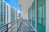 Private covered balcony with stone-finish flooring, full-height glass panel walls, and metal mesh railing