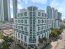 Mid-rise urban building featuring a stepped architectural design, glass balcony railings, floor-to-ceiling windows, and white concrete exterior finish