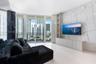 Kitchen featuring light wood-finish cabinetry, black stone-patterned backsplash, quartz-topped peninsula with stone-finish waterfall edge, stainless s